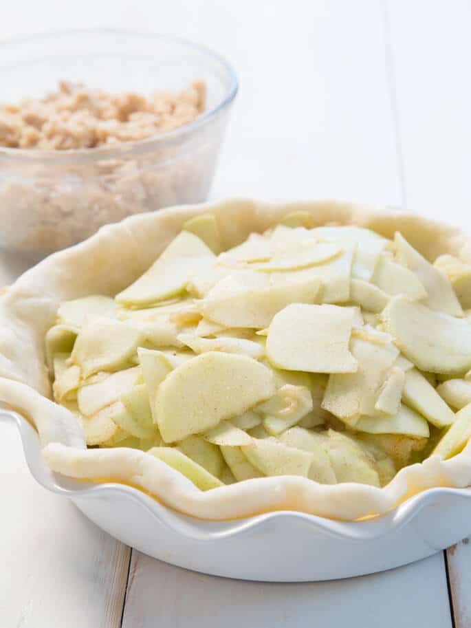 Un gros plan de pâte à tarte avec des pommes et de la cannelle à l'intérieur d'une plaque de cuisson blanche