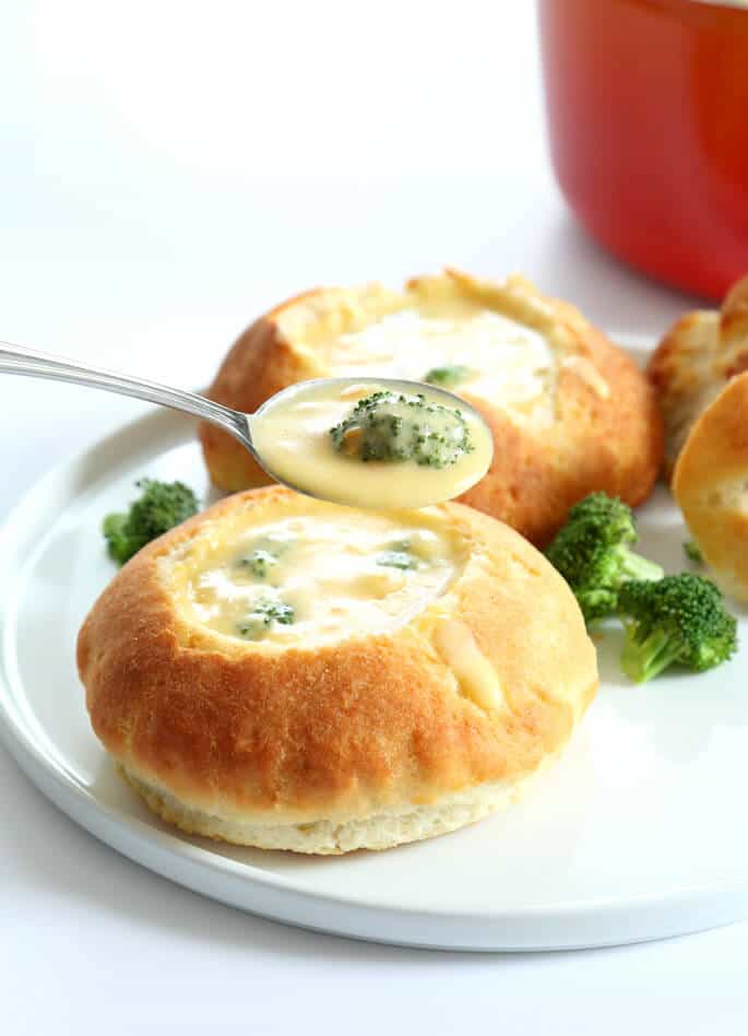 Broccoli cheddarsoppa i brödskål med broccoli på vit tallrik och närbild av soppan i en sked