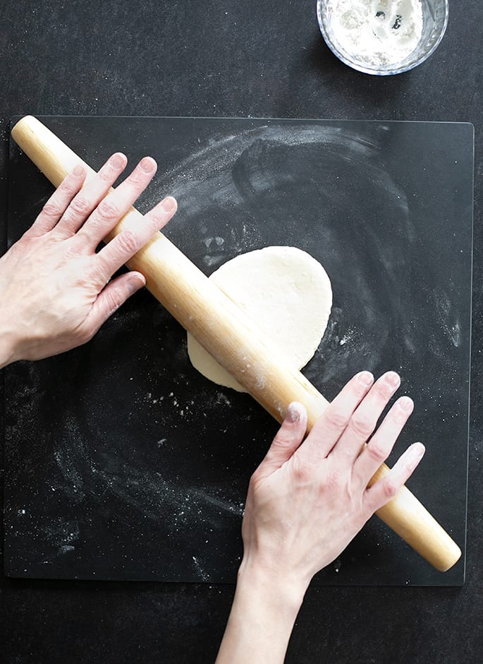 Overhead image of hands rolling out oval dough with a rolling pin