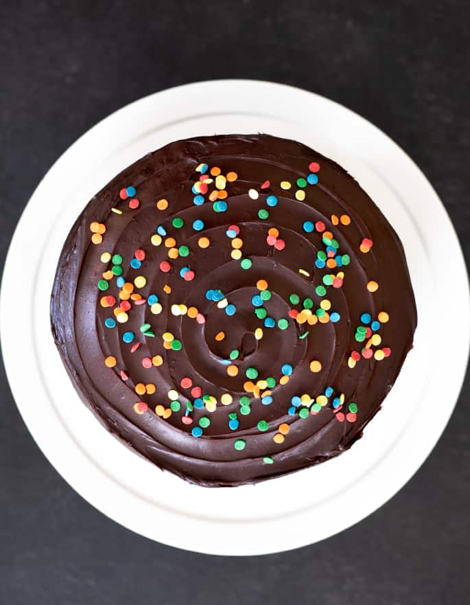 Este clássico bolo de aniversário sem glúten é um bolo em camada de baunilha funfetti recheado com cobertura de creme de chocolate e coberto com cobertura de chocolate. É o seu novo bolo de aniversário de go-to-bolo.