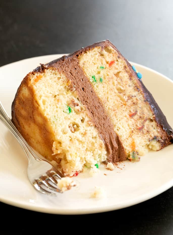 Dieser klassische glutenfreie Geburtstagskuchen ist ein Funfetti-Vanille-Schichtkuchen, der mit Schokoladen-Sauerrahm-Glasur gefüllt und mit Schokoladenglasur gekrönt ist. 