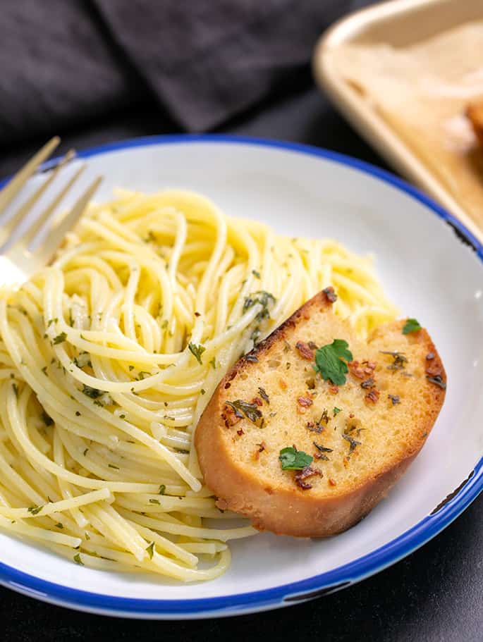 Spagetti valkoisella lautasella haarukan ja valkosipulileivän palan kanssa