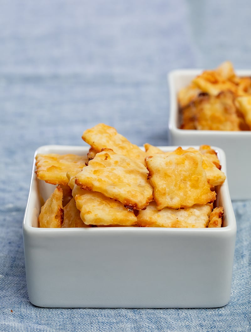 Square cheese crackers in small square white dish on blue cloth