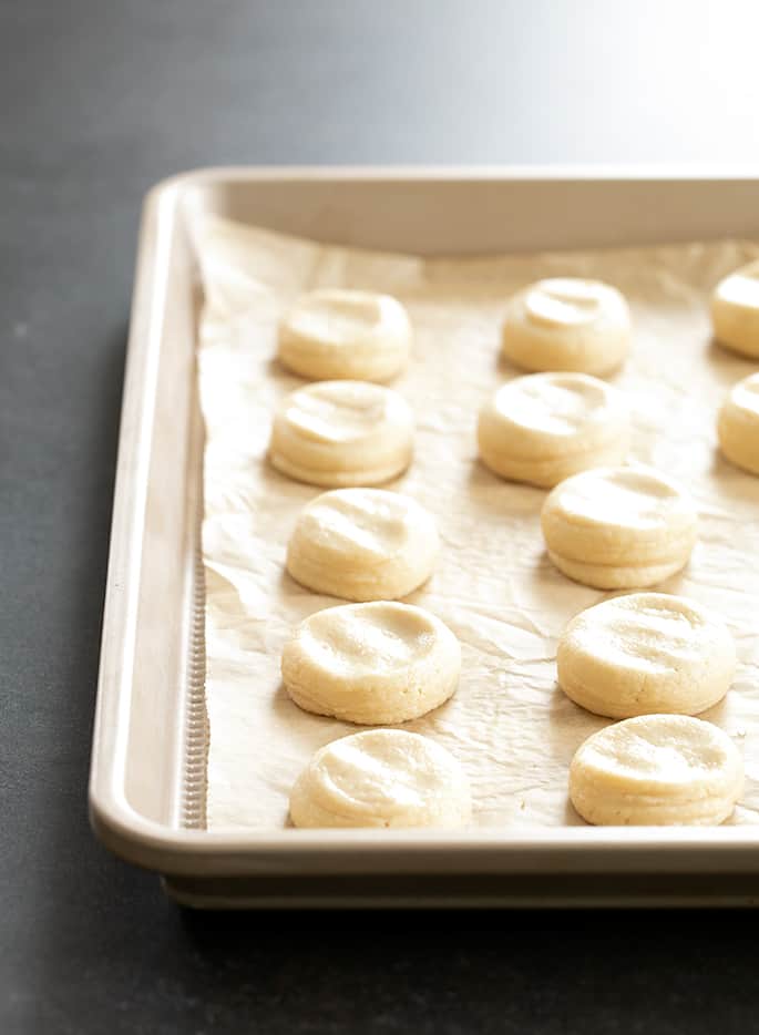 Light yellow mounds of vanilla wafers raw on gold baking tray lined with brown paper