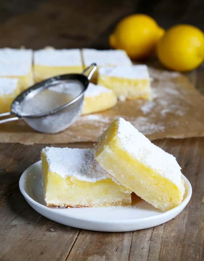 A small white plate with two lemon squares and powdered sugar