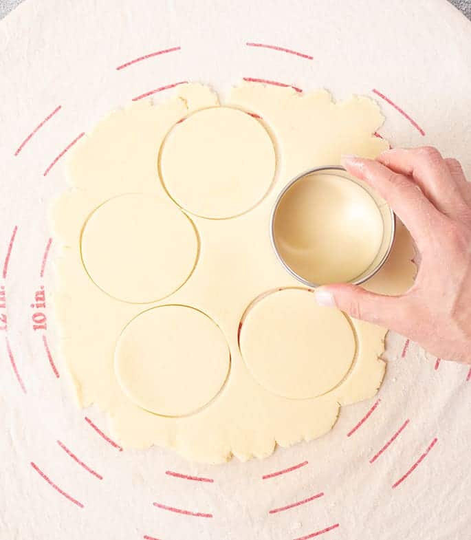 Hand holding round cutter making cuts in dough