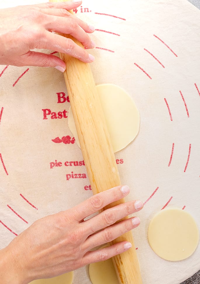 Hands holding rolling pin rolling out rounds of dough