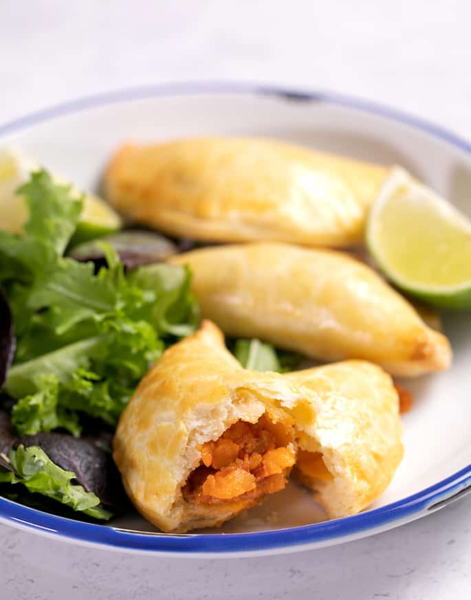 Plate of empanadas and greens with on empanada broken in half