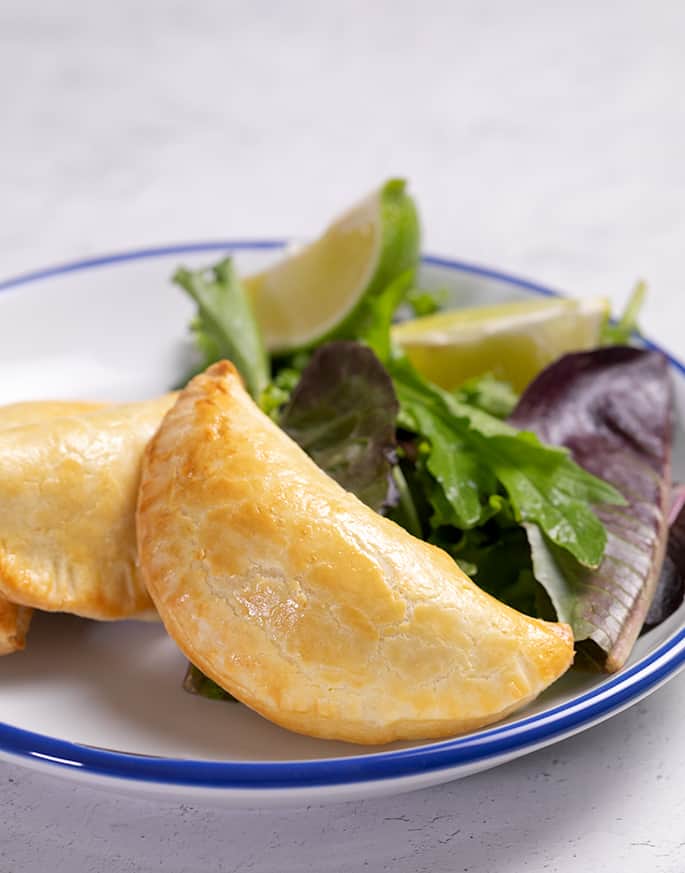 Three empanadas on a white plate with greens and a lime wedge