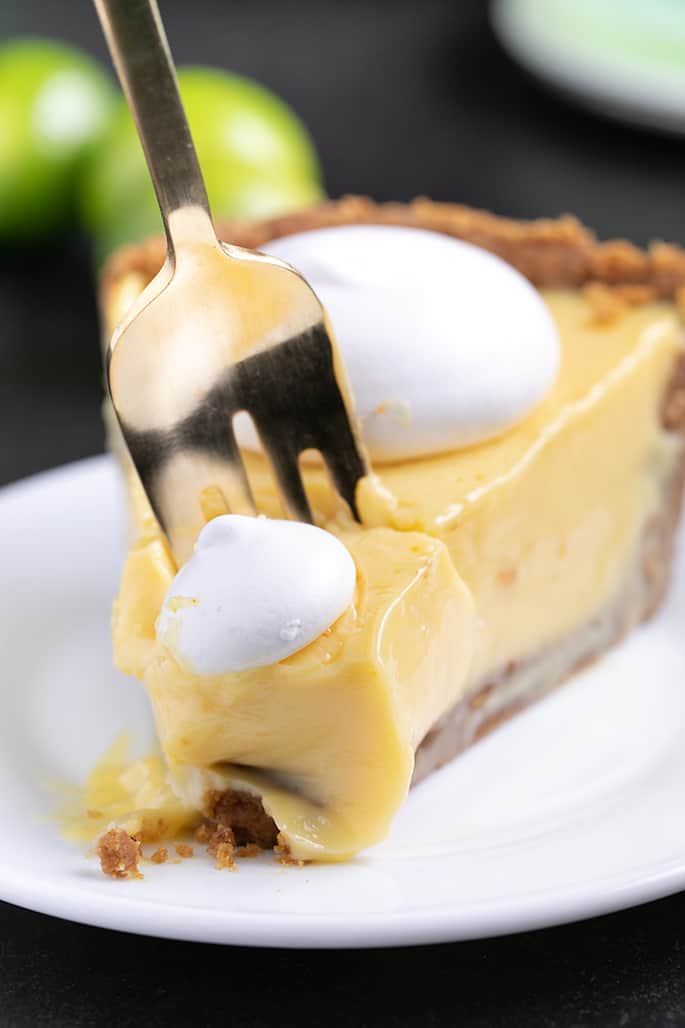 Tines of gold colored fork going into end of slice of key lime pie