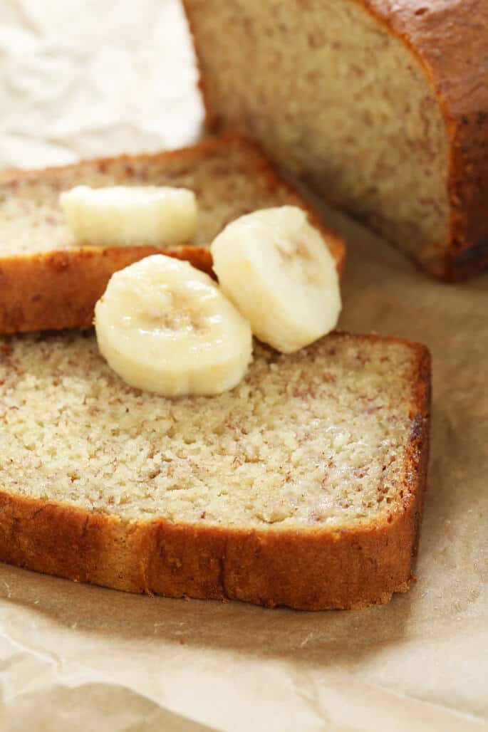 Closeup of a slice of light brown quick bread with 3 slices of fresh bananas on brown paper