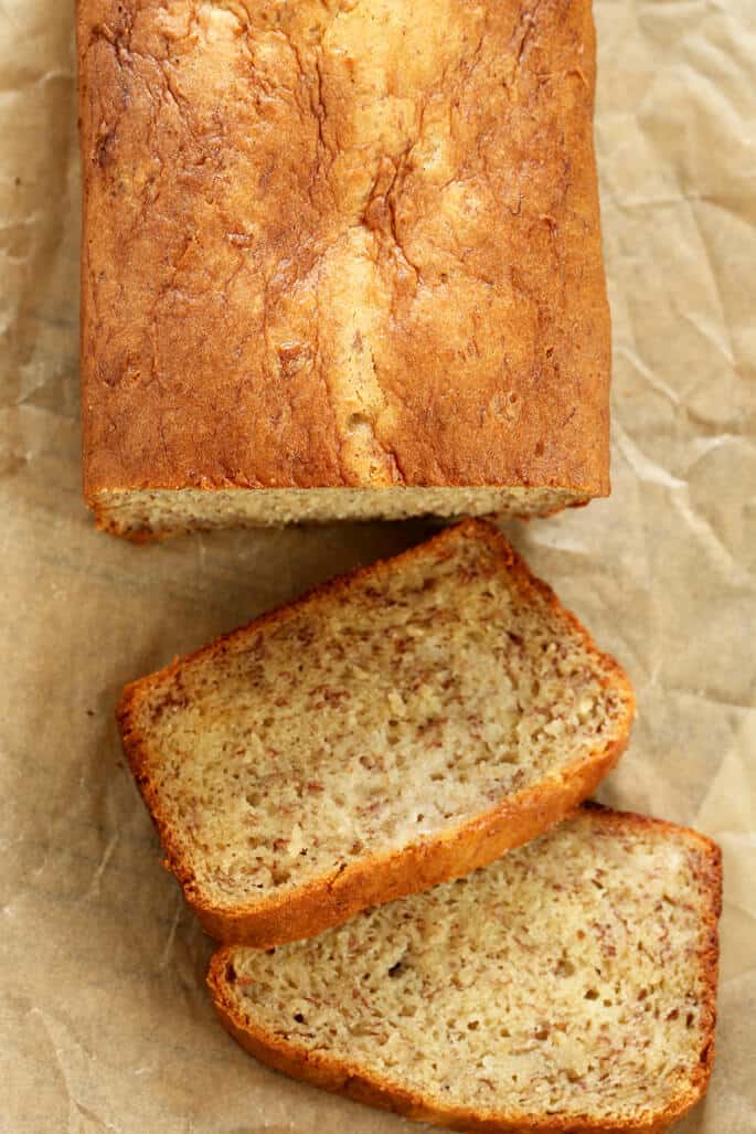 Overhead image of 2 slices and rest of loaf of gluten free banana bread with darker brown flecks on brown paper