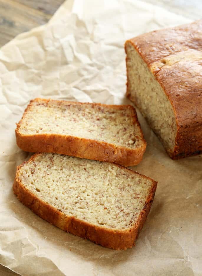 2 slices of light brown gluten free banana bread with darker brown flecks and deep brown crust on crinkled brown paper