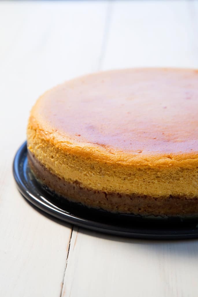 A close up of the side view of pumpkin cheesecake on black platter