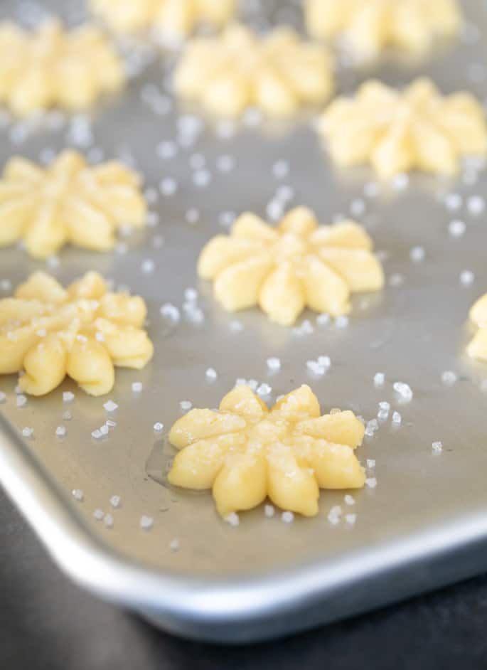 Raw gluten free butter cookies in a flower shape on a tray.