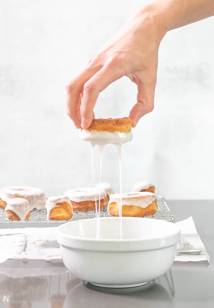 A hand with a donut dripping glaze