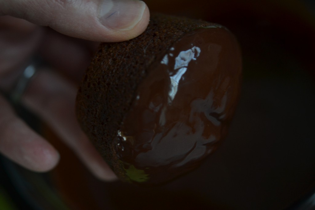 A cupcake being dipped in chocolate sauce 