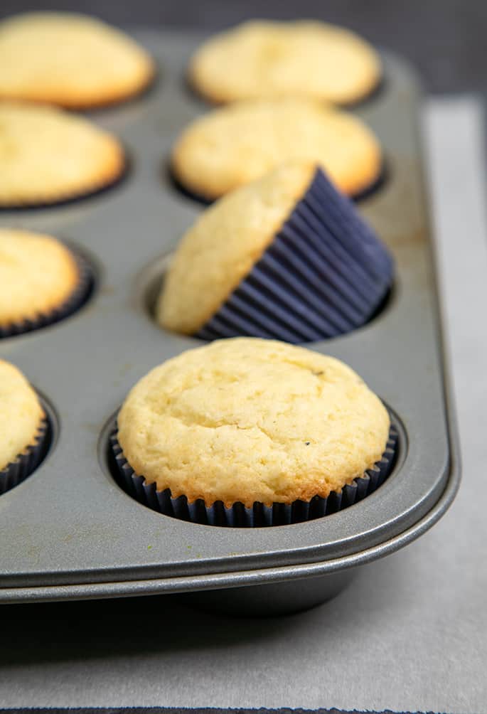 Baked cupcakes in blue liners in muffin tin on white paper