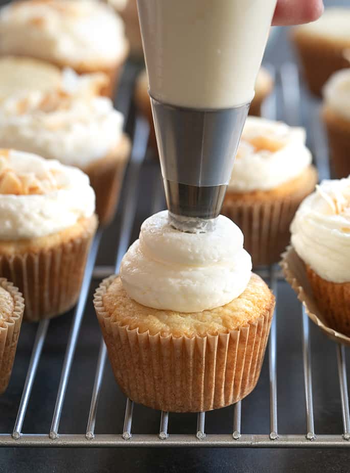 A close up of frosting coming out of a piping bag onto a coconut cupcake