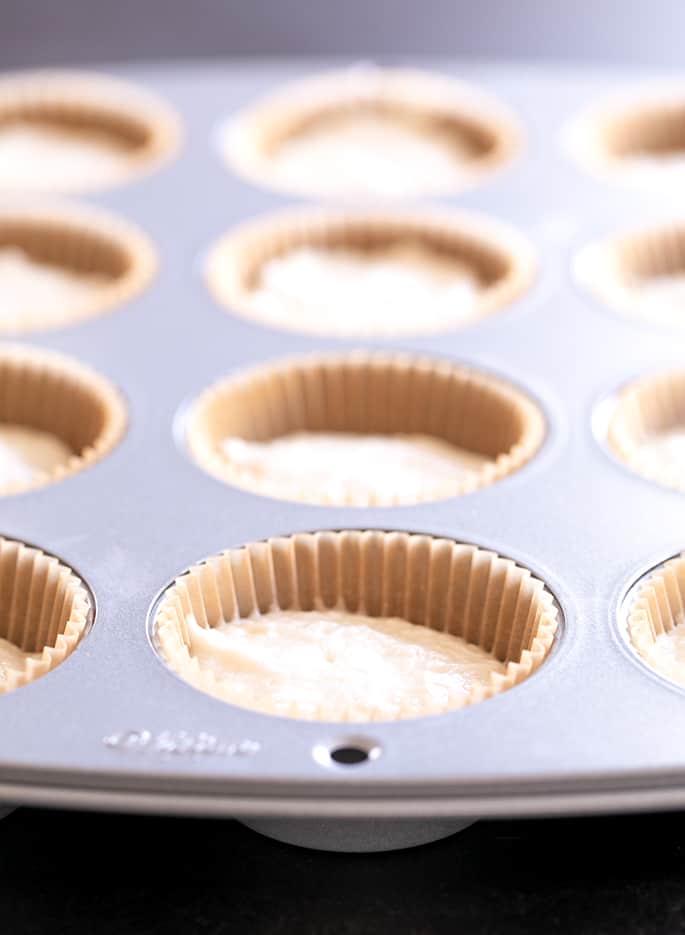 A muffin tin with liners and batter filling wells