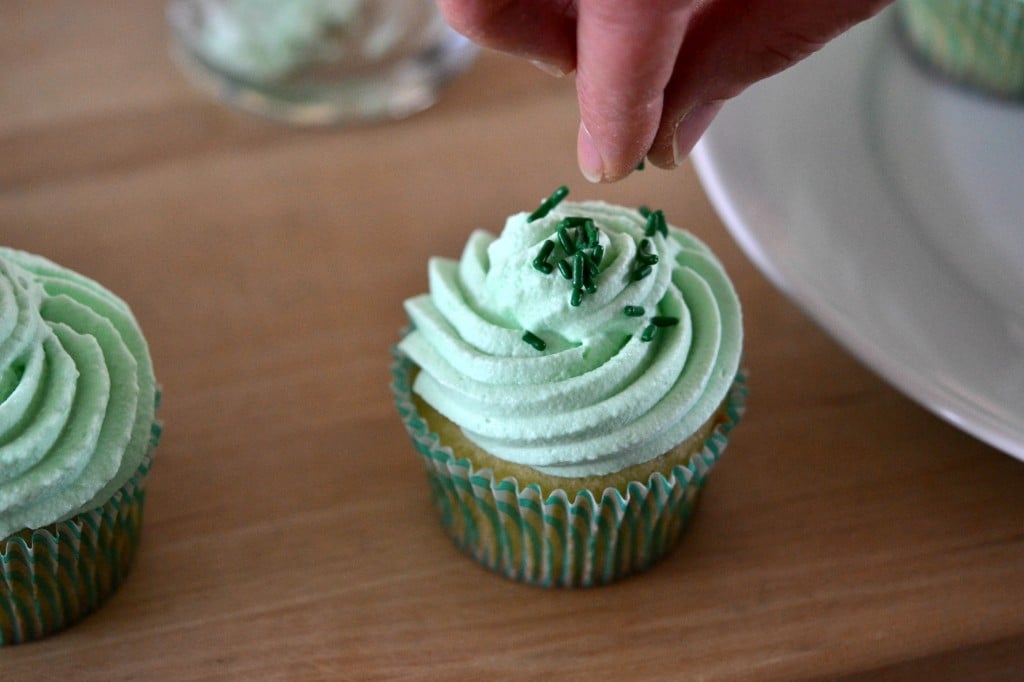 A close up of a person decorating Shamrock Shake Cupcakes