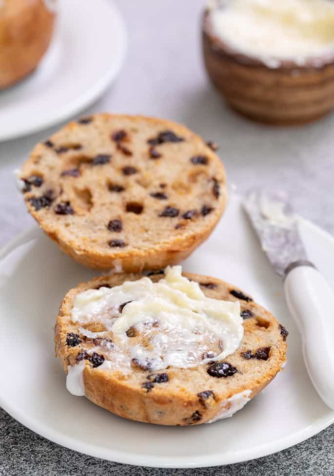 Hot cross bun split in half with butter and butter knife on small white plate