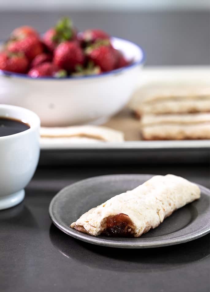 A bitten Nutri grain bar on a plate with a cup of coffee