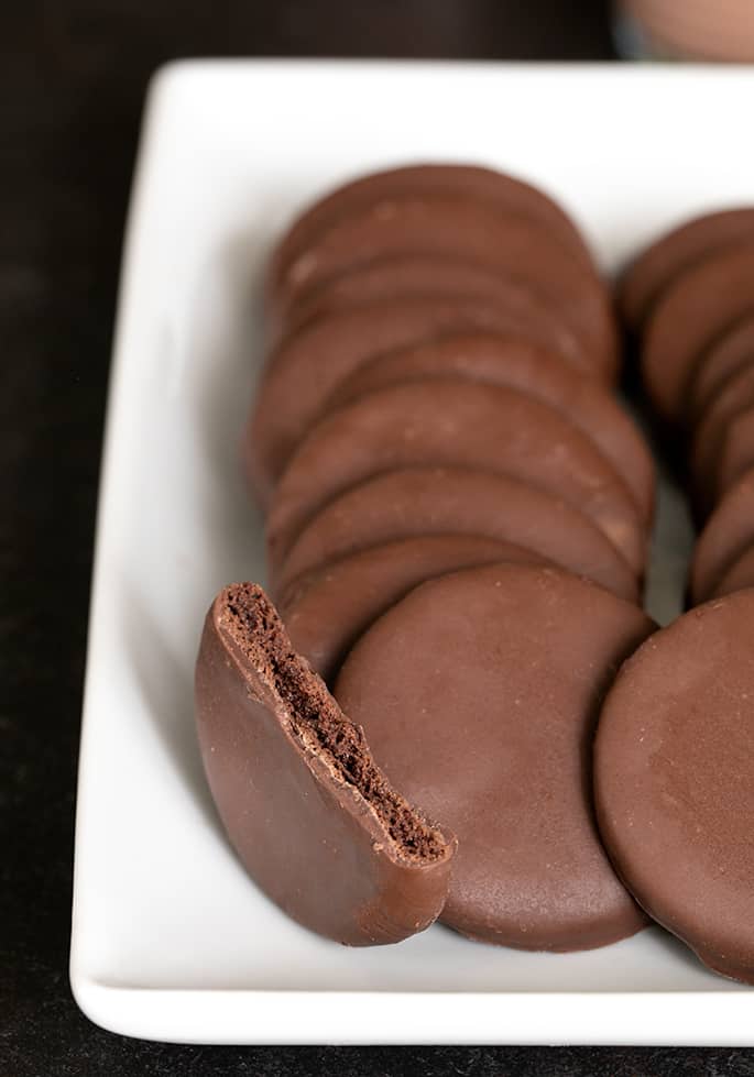 A closeup image of gluten free thin mints cookies plated with one broken cookie to show inside.