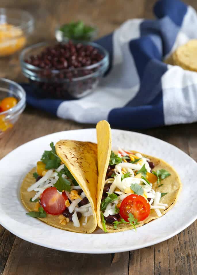 Two fresh corn tortillas with tomatoes, beans, cheese, and parsley