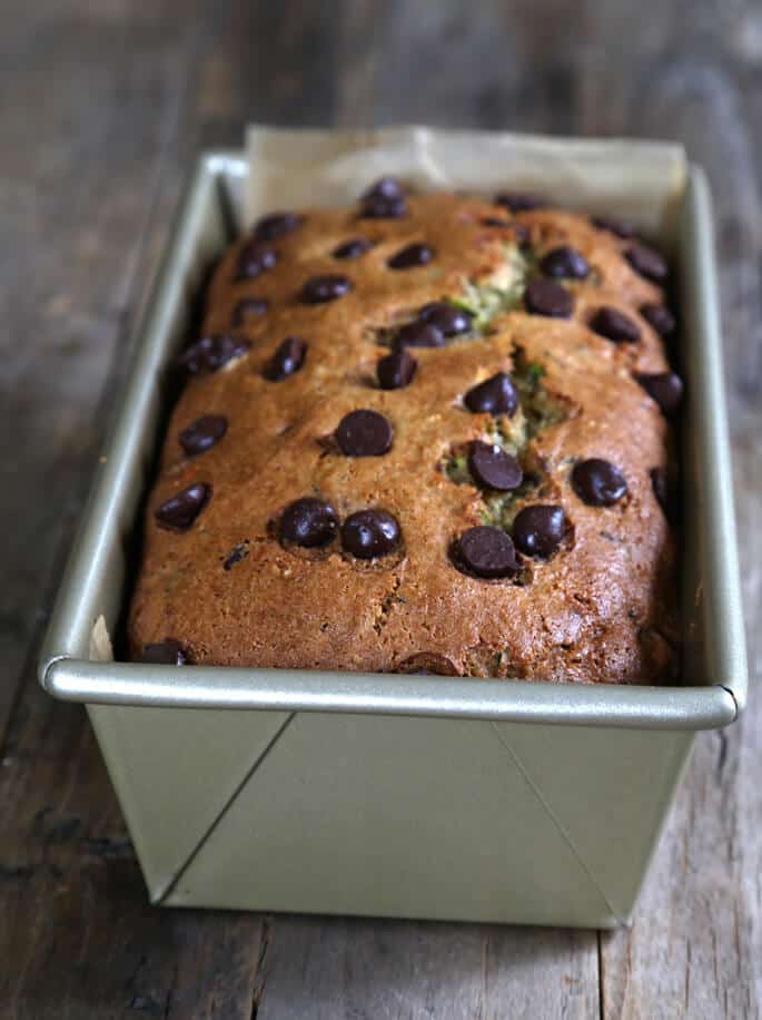 brown crust of gluten free zucchini bread with chocolate chips on top in light gold colored metal loaf pan on brown table