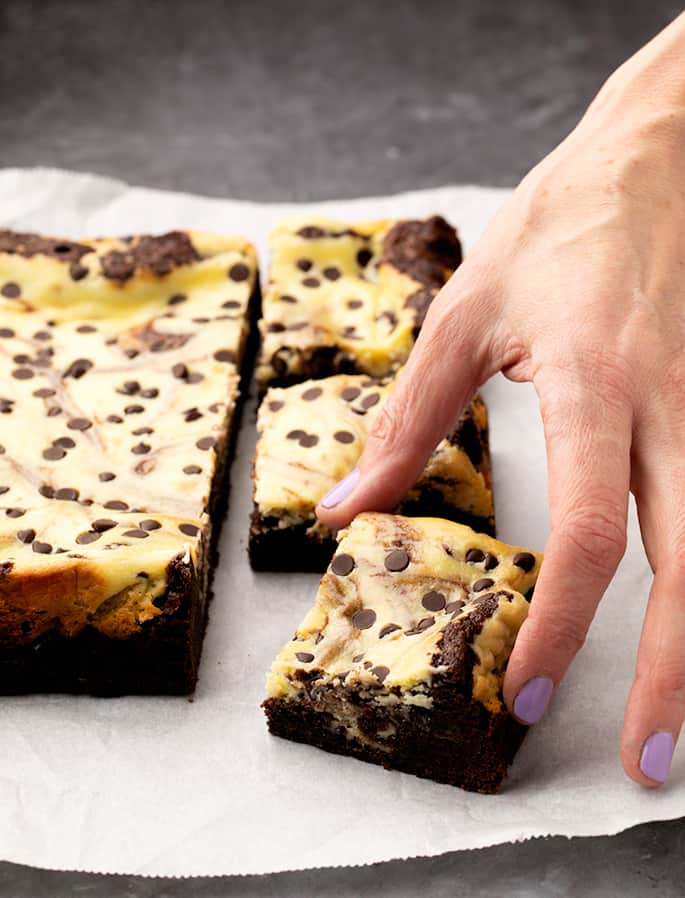 Fingers picking up a marble brownie square from the rest on white paper