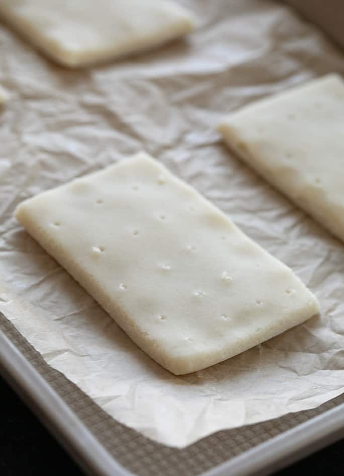 Shaped, raw gluten free pop tarts with a brown sugar and cinnamon filling, on the baking tray ready to bake. 