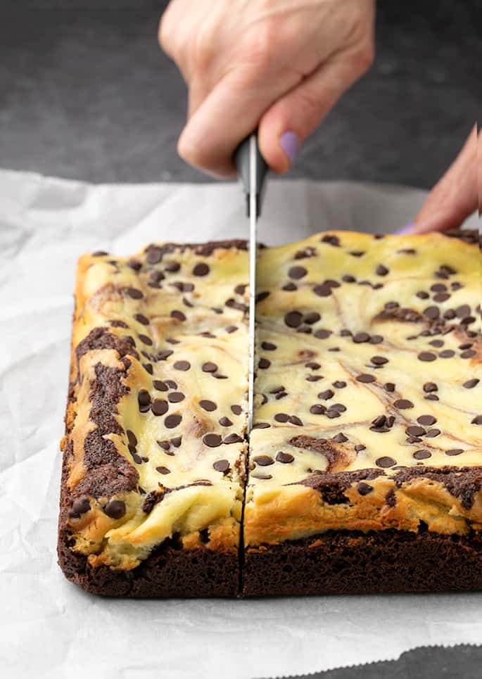 Hand holding knife cutting marble brownies on white paper