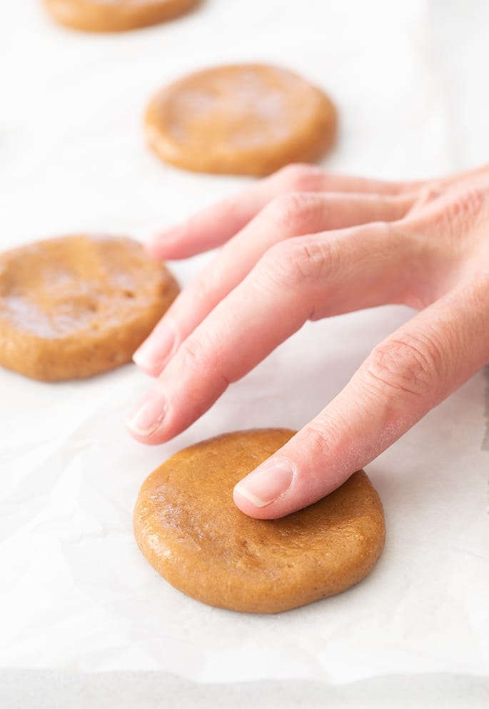 Fingers flattening mounds of molasses cookie dough