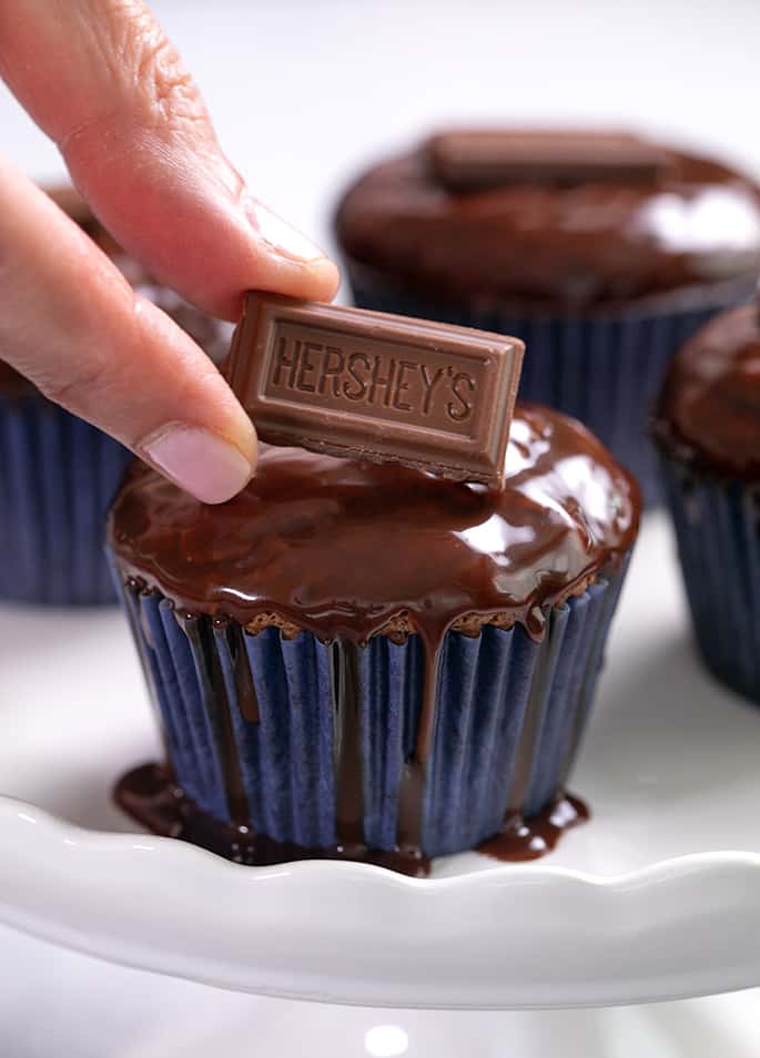 Fingers placing piece of Hershey's milk chocolate on a glazed cupcake