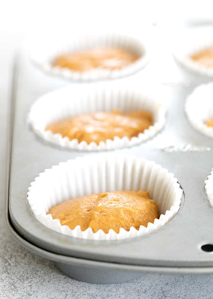 Pumpkin cupcake batter in muffin tin with white liners