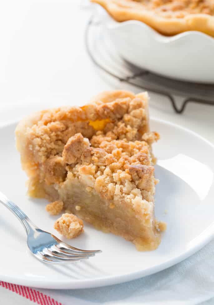 A close up of dutch apple pie on a white plate with a fork 