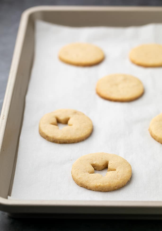 Baked linzer cookies some with cutouts on white paper on tray