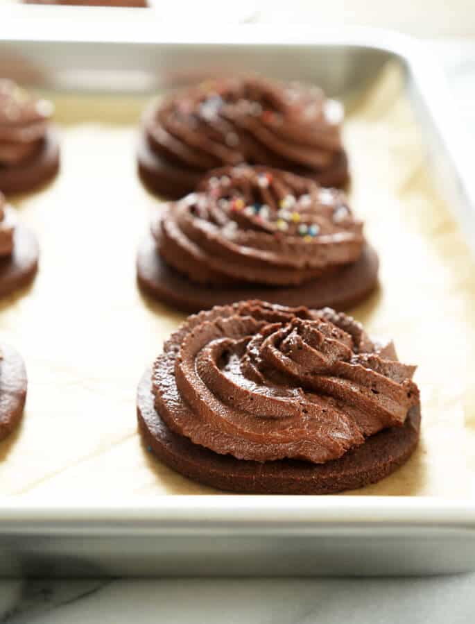 A close up of a chocolate cutout cookie with chocolate frosting on beige paper