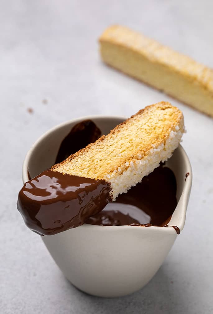 Chocolate dipped sugar-encrusted biscotti on top of small pitcher of melted chocolate