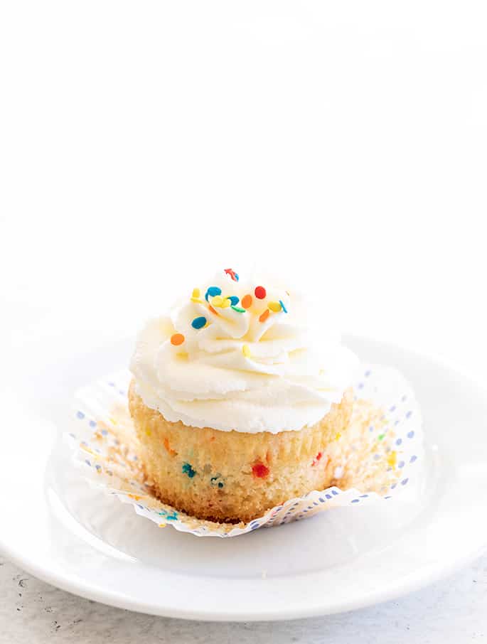 Single gluten free funfetti cupcake on a plate with wrapper peeled