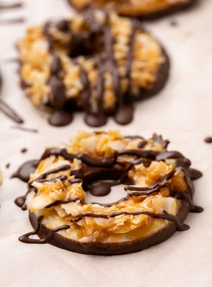 Chocolate-dipped Samoas-style cookies from the side on white paper