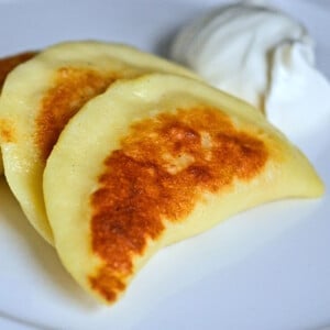 3 gluten free pierogi on white plate with sour cream