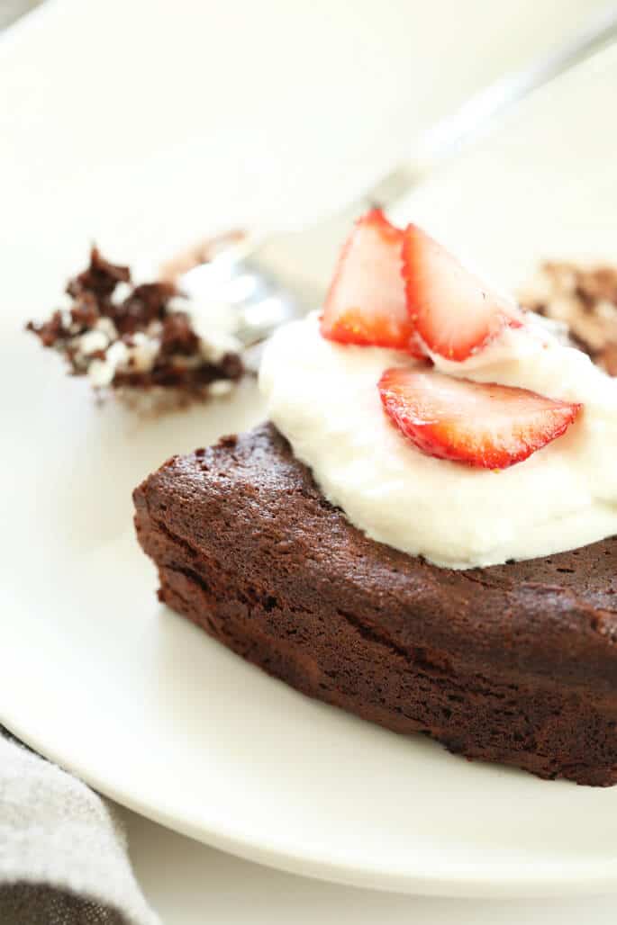 A slice of flourless chocolate cake on a plate with a fork with cake on it