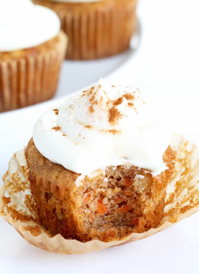 Light brown/orange colored cupcake with light brown wrapped pulled down, topped with white frosting with dusting of brown ground spice