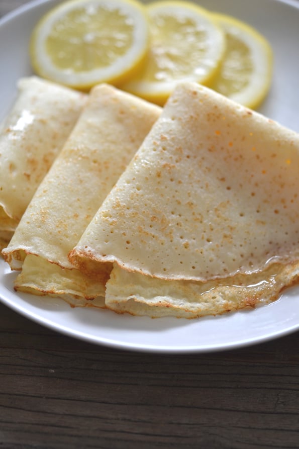 3 crepes su un piatto bianco con 3 fette di limone sullo sfondo