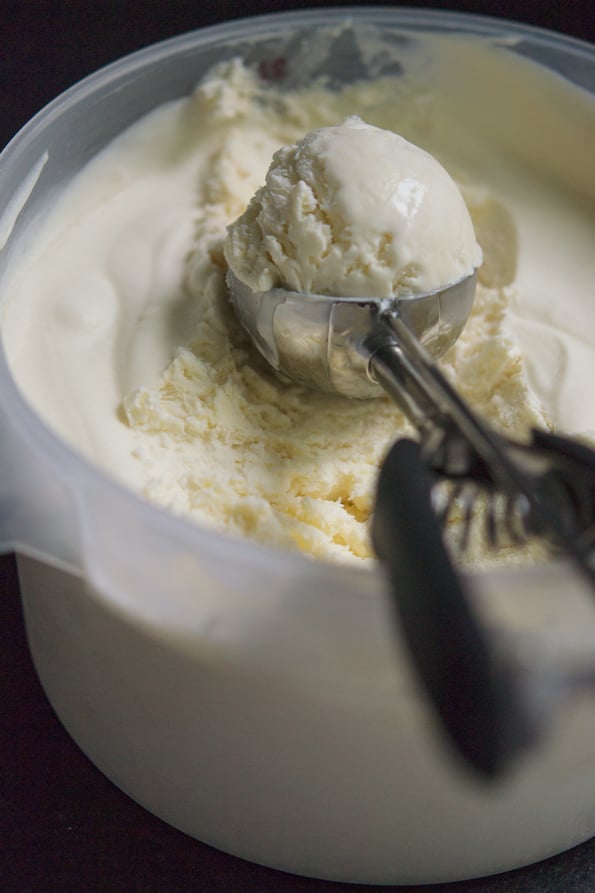 An ice cream scoop with vanilla ice cream in a bucket of more ice cream