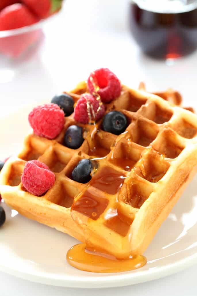 A close up of a waffle with raspberries, blueberries and syrup