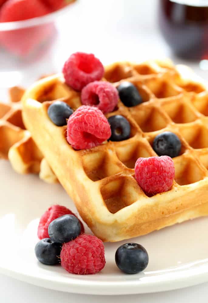 A close up of a waffle with raspberries and blueberries