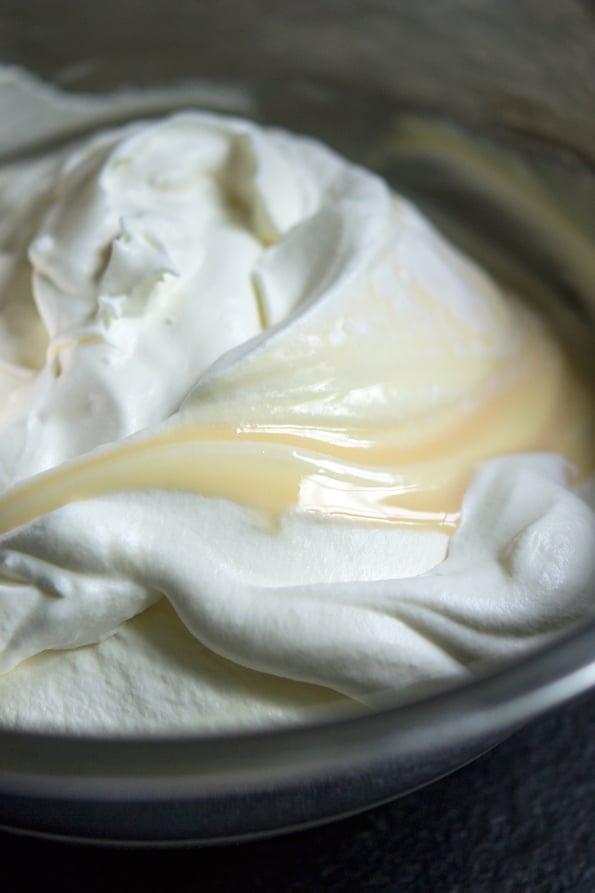 A large glass mixing bowl with whipped cream and sweetened condensed milk